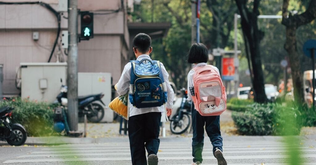 Two kids with backpacks crossing the street to school